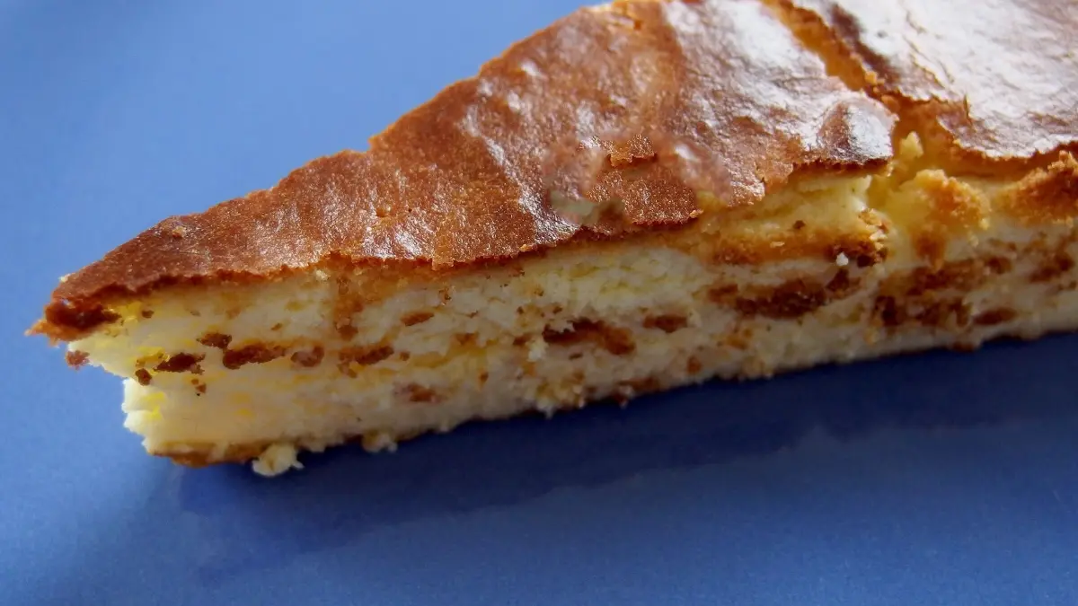 Ein K&auml;sekuchen ohne Boden liegt auf einem blauen Teller und zeigt eine goldbraune, leicht gebr&auml;unte Oberfl&auml;che.