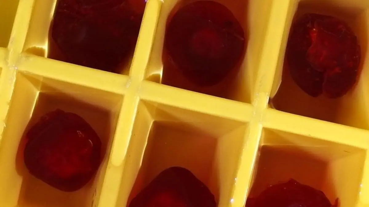 Kugelf&ouml;rmige, rote Eisw&uuml;rfel liegen in einem gelben Eisw&uuml;rfelformer in einer k&uuml;hlen Umgebung, bereit zum Servieren.