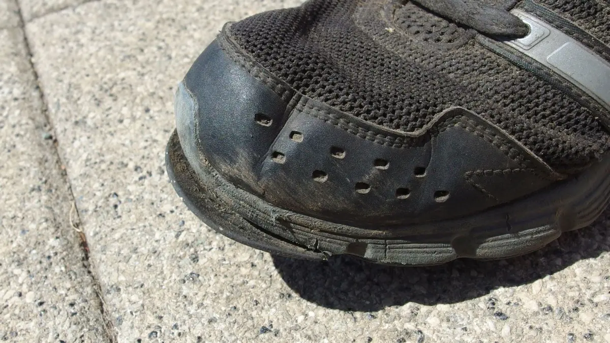 Ein Schuh mit abgel&ouml;ster Sohle steht auf einer grauen Fl&auml;che. Der Zustand weist Abnutzung und Besch&auml;digungen auf.