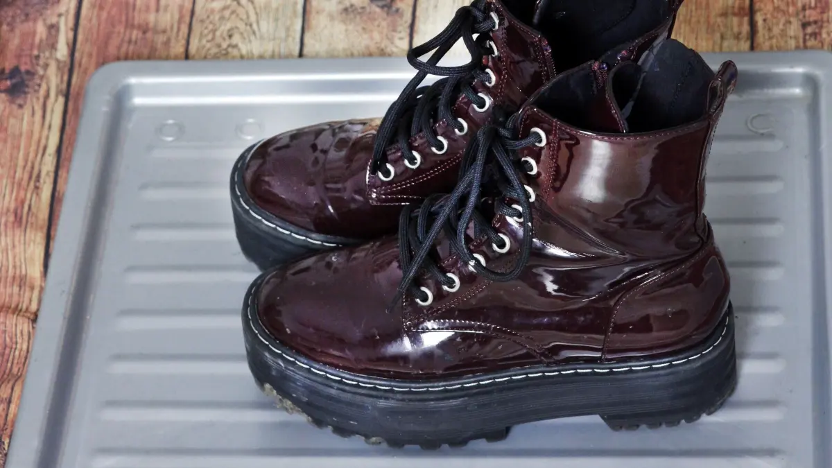 Dunkelrote Stiefel stehen auf einer silbernen Ablage f&uuml;r schmutzige Schuhe, um Schmutz zu sammeln.