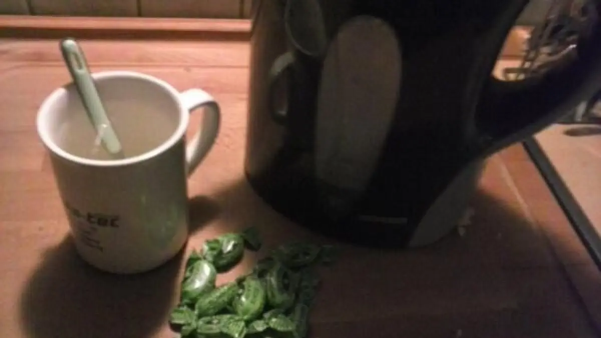 Eine Tasse steht neben einem Wasserkocher, w&auml;hrend gr&uuml;ne Hustenbonbons auf der Holzoberfl&auml;che liegen, bereit zur Verwendung.