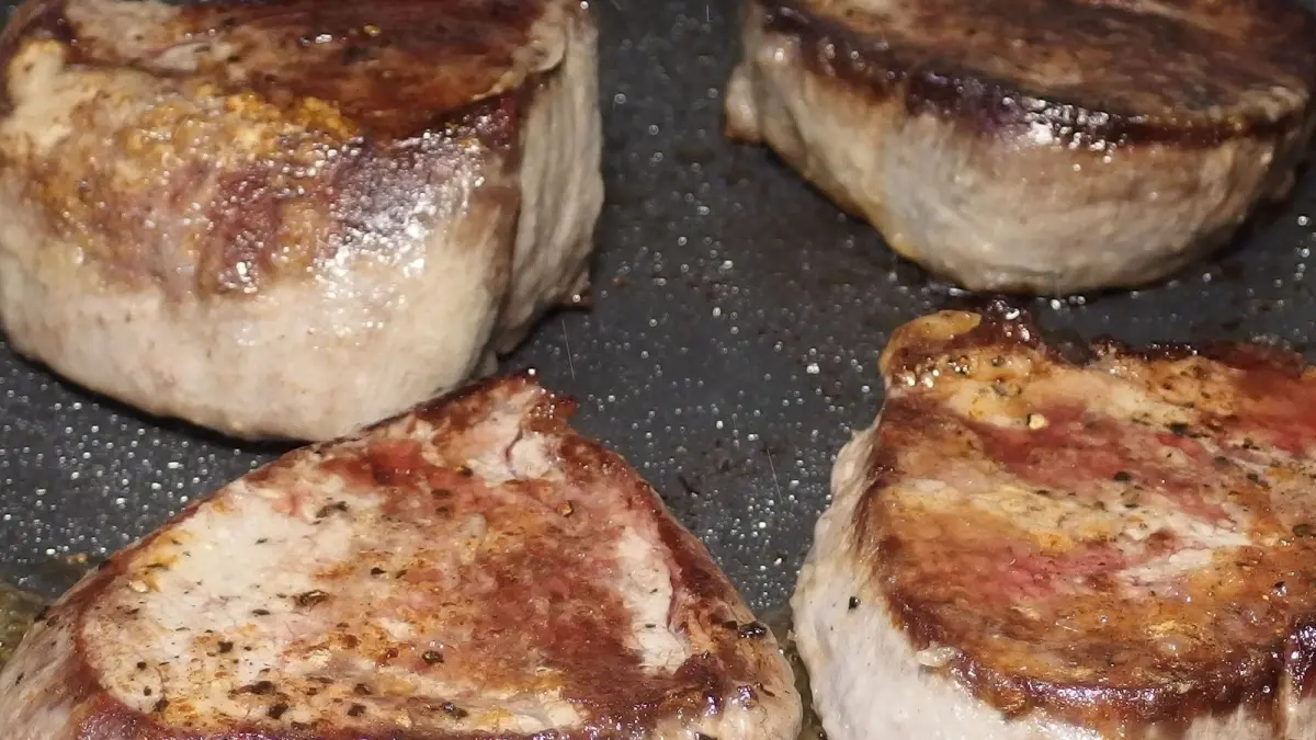 Saftige Steaks braten in einer Pfanne, goldbraun und knusprig, auf einem dunklen Hintergrund.