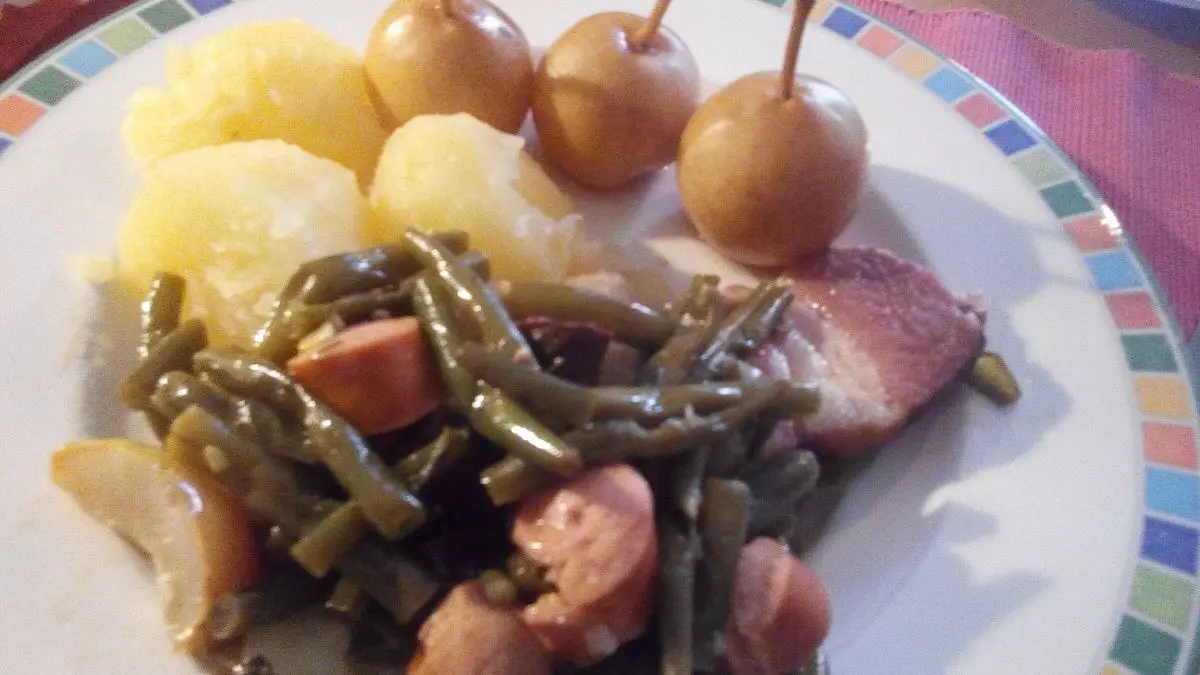 Ein Teller mit Birnen-Bohnen und Speck zeigt gr&uuml;ne Bohnen, Kartoffeln und Speck neben s&uuml;&szlig;en Birnen auf farbigem Geschirr.