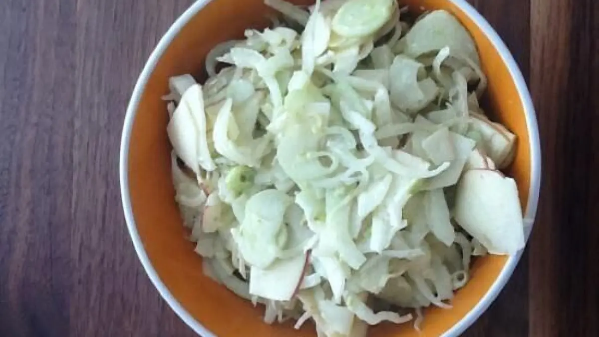 Ein Sch&uuml;ssel voller verblasster Fenchelbl&auml;tter liegt mittig auf einem Holzuntergrund. Der Fenchelsalat ist frisch zubereitet.