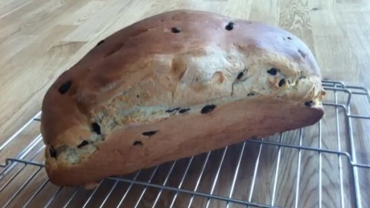 Rosinenbrot k&uuml;hlt auf einem Gitter auf einem Holztisch ab, mit goldbrauner Kruste und sichtbaren Rosinen im Teig.
