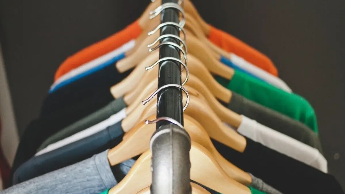 Bunte T-Shirts h&auml;ngen ordentlich an einem Kleiderst&auml;nder, w&auml;hrend ein gro&szlig;er Kalender an der Wand im Hintergrund sichtbar ist.