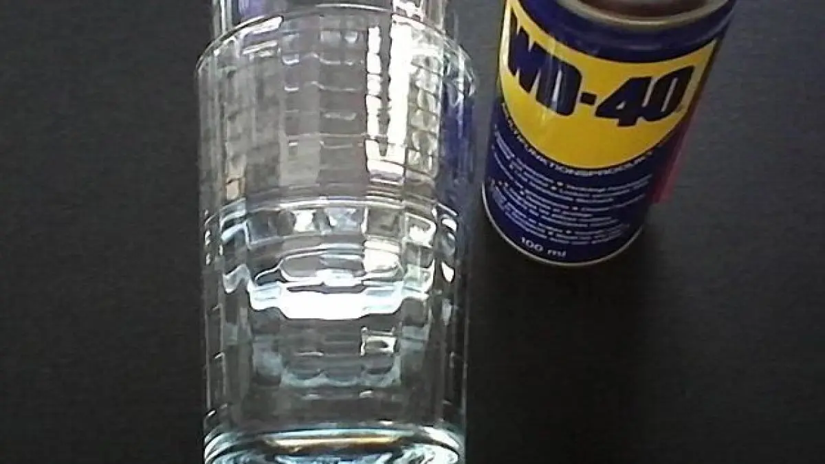 Ein WD-40 Spray steht neben einem leeren Glas auf einem schwarzen Tisch, bereit f&uuml;r vielf&auml;ltige Anwendungen im Haushalt.