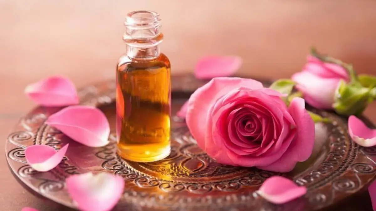 Ein Glasfl&auml;schchen mit goldenem Parf&uuml;m steht auf einem dekorativen Tablett neben einer rosa Bl&uuml;te und Rosenbl&auml;ttern.