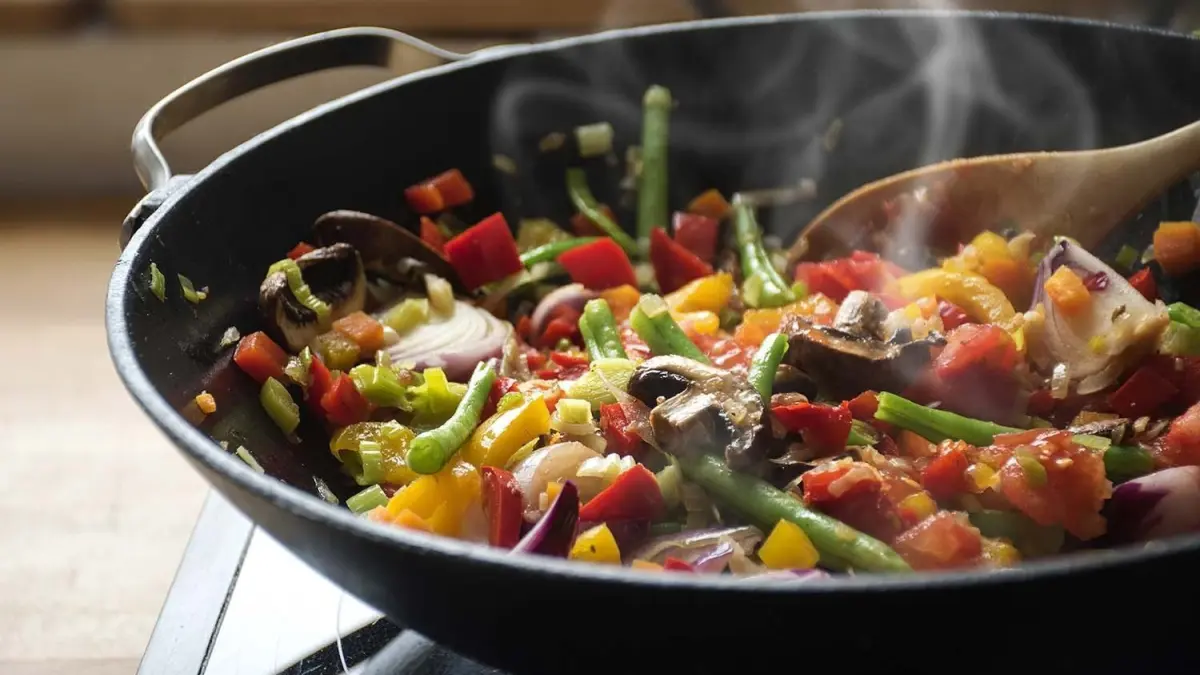Bunte Gem&uuml;sepfanne auf dem Herd, w&auml;hrend sie dampfend ger&uuml;hrt wird, um leicht angebranntes Essen zu retten.