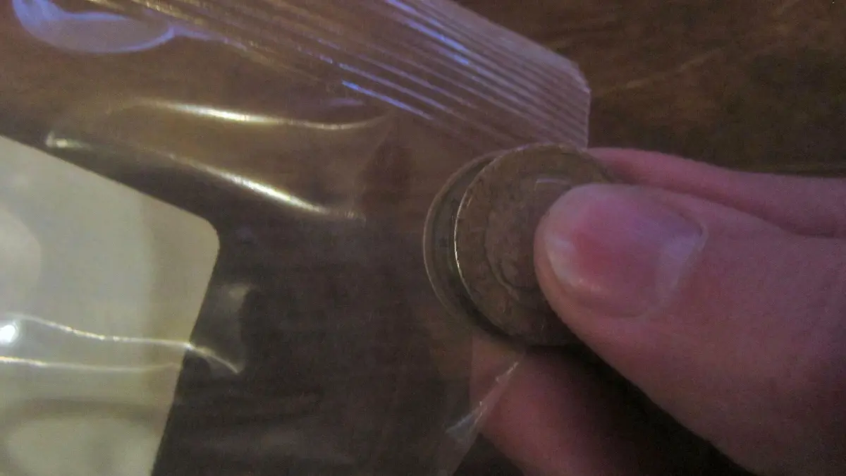 Ein Finger h&auml;lt eine M&uuml;nze, die in eine Plastikverpackung gedr&uuml;ckt wird, um sie ohne Schere zu &ouml;ffnen.
