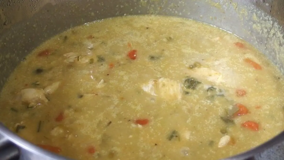 Ein Topf mit H&auml;hnchen-Restverwertung kocht eine dicke, gr&uuml;ne Suppe mit Gem&uuml;se und St&uuml;ckchen von H&auml;hnchen.