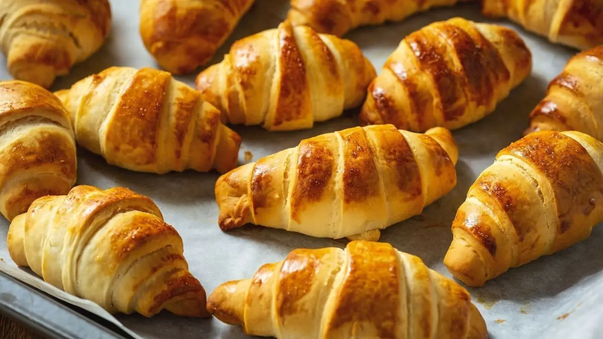 Luftige Croissants liegen frisch gebacken auf einem Backblech, goldbraun und appetitlich, im warmen K&uuml;chenambiente.