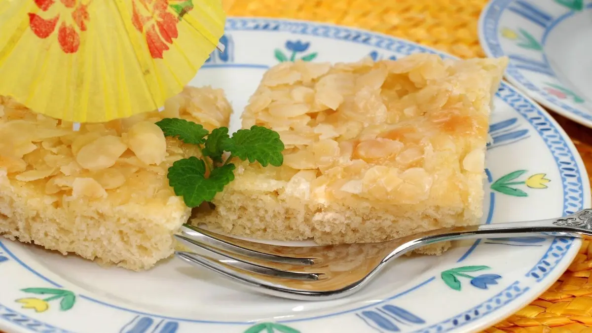 Butterkuchen auf einem Teller, ein St&uuml;ck ist mit einer Gabel angeschnitten, darum frische Minze und eine dekorative Ananasfigur platziert.