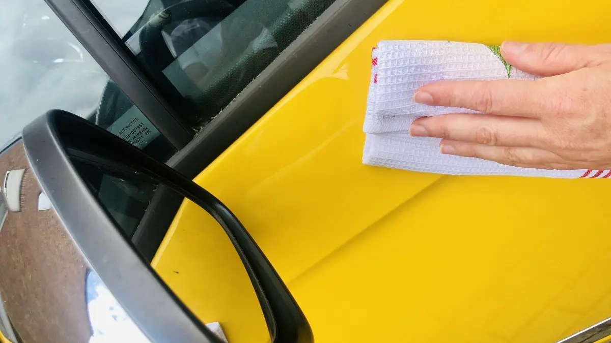 Ein gelbes Auto wird mit einem Tuch poliert, um den Klarsp&uuml;ler aufzutragen und es auf Hochglanz zu bringen.