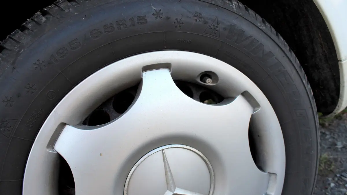 Ein silberner Alufelgen eines Mercedes auf einem Reifen, der in einem Au&szlig;enbereich steht, wirkt leicht verschmutzt.