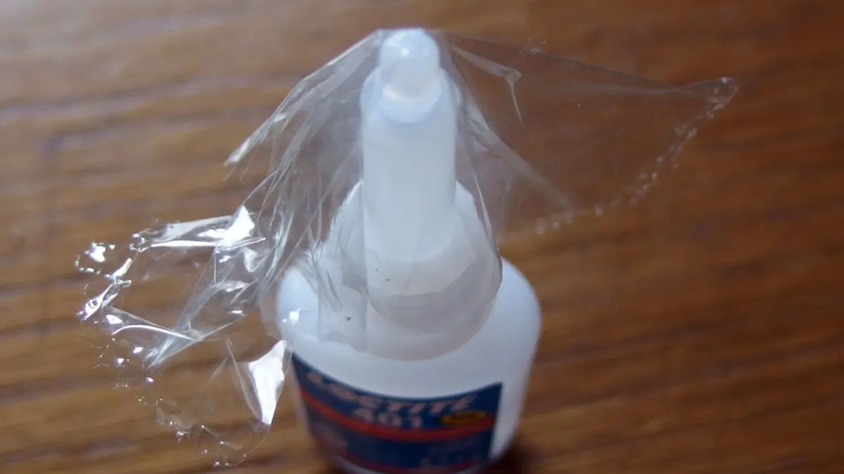 Ein Fl&auml;schchen Sekundenkleber steht auf einem Tisch, w&auml;hrend das Verschlusspl&auml;ttchen noch eingesetzt ist und eine &Ouml;ffnung verhindert.