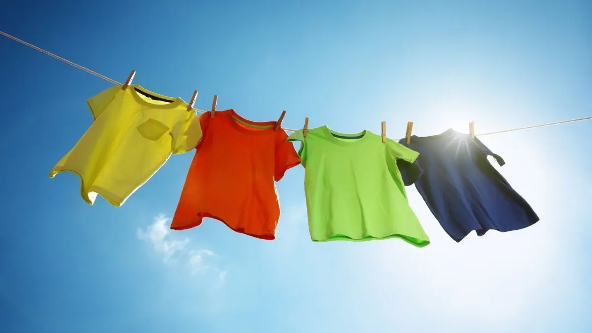 Bunte Sportshirts h&auml;ngen an einer W&auml;scheleine, w&auml;hrend die Sonne strahlt und den klaren Himmel beleuchtet.