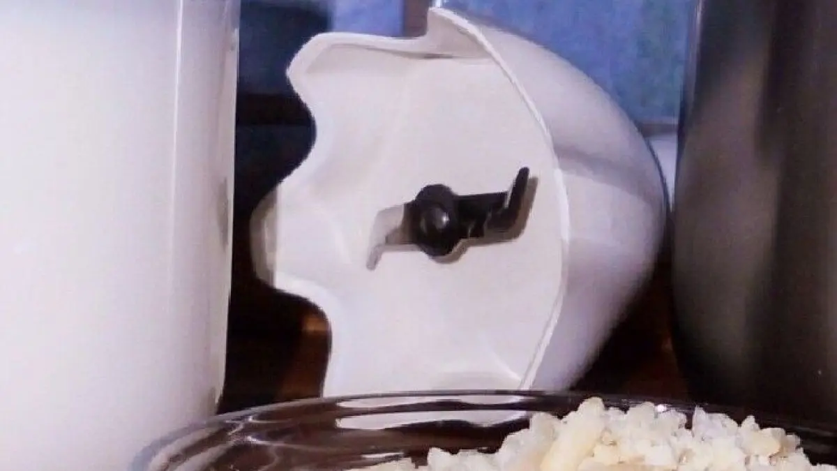 Ein Glas Mandel-Reismilch steht neben einem Mixbeh&auml;lter und einer Sch&uuml;ssel mit geriebenem Reis auf einer Holzoberfl&auml;che.