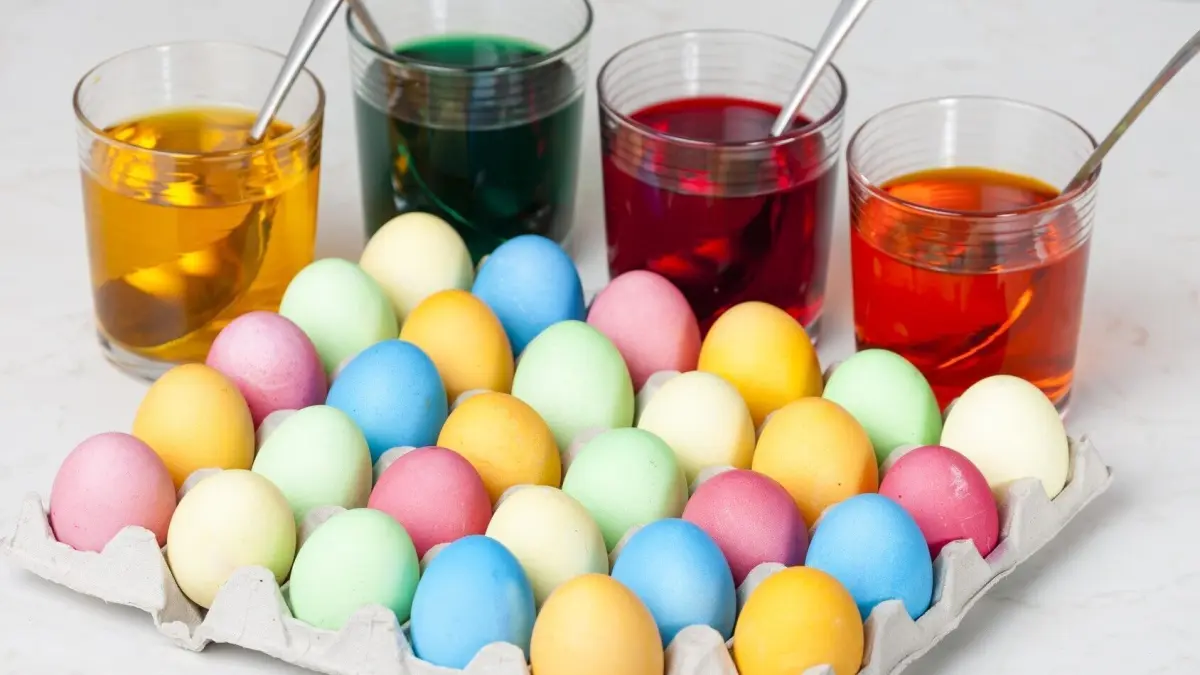 Bunte Ostereier liegen in einem Eierschacht und werden in T&ouml;pfen mit verschiedenen Farben getaucht.