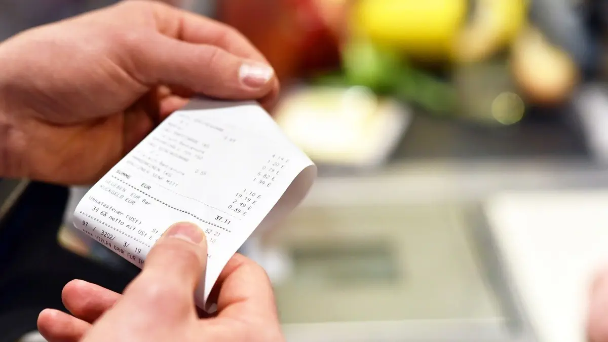 Eine Person h&auml;lt einen Kassenzettel in der Hand, w&auml;hrend im Hintergrund frisches Obst sichtbar ist, was auf Umtauschm&ouml;glichkeiten hinweist.