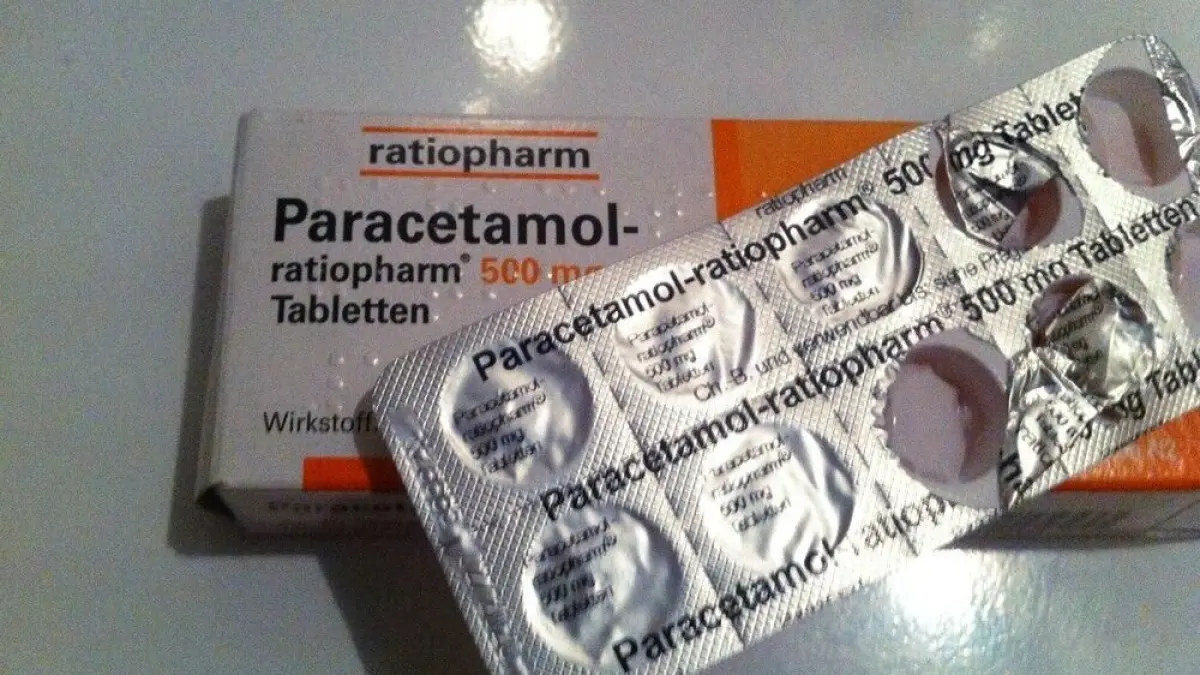 Paracetamol-Tabletten liegen neben einer offenen Blisterpackung auf einem wei&szlig;en Tisch, bereit zur Anwendung gegen Schwei&szlig;flecken.