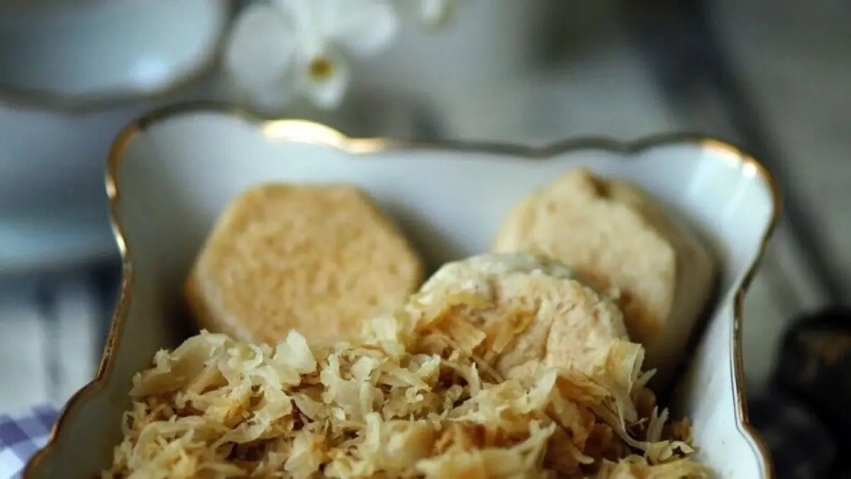 In einer eleganten Sch&uuml;ssel liegen warme Dampfkn&ouml;del mit knackigen Br&ouml;tchen, umgeben von aromatischem Sauerkraut.