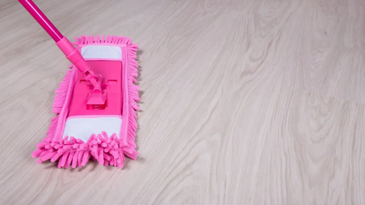 Ein pinker Wischmopp reinigt einen Laminatboden in einem hellen Raum, der Geradlinigkeit und Sauberkeit vermittelt.