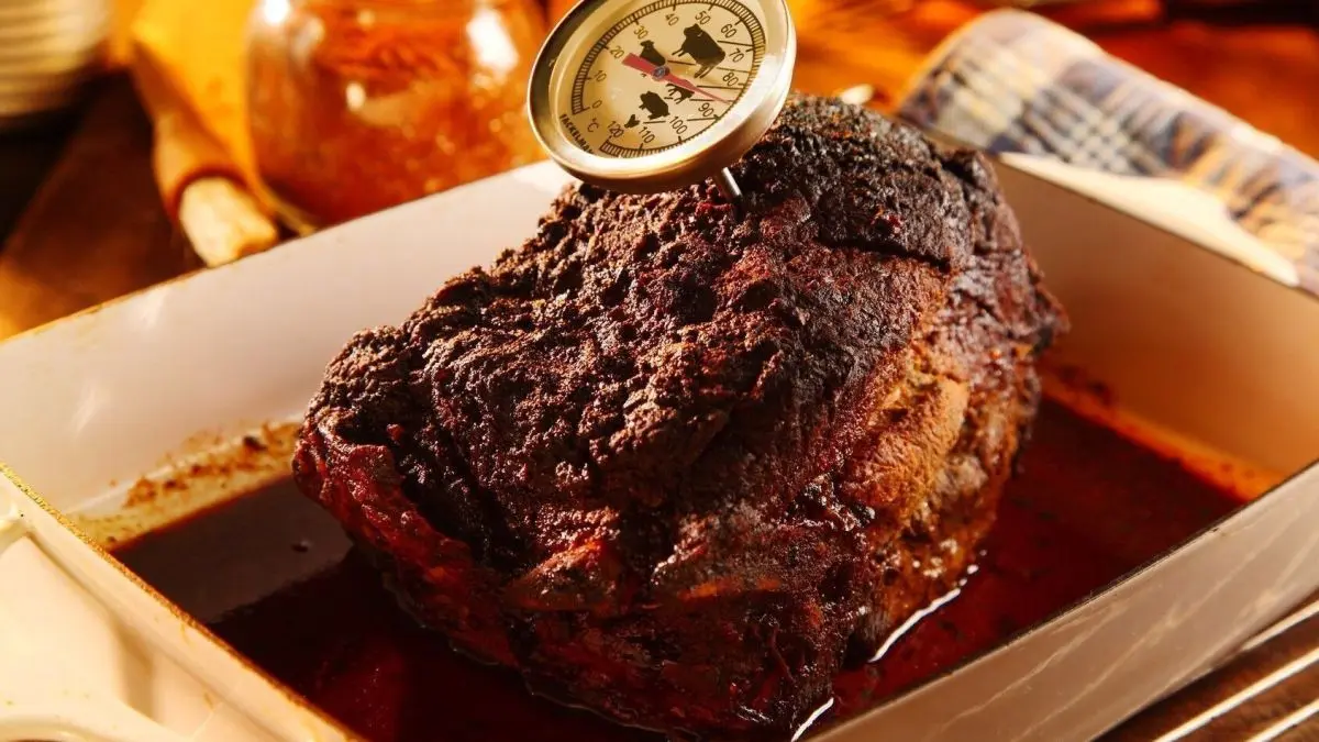 Ein saftiger Braten liegt in einer Schale, w&auml;hrend ein Thermometer die Temperatur beim Niedrigtemperaturgaren misst.