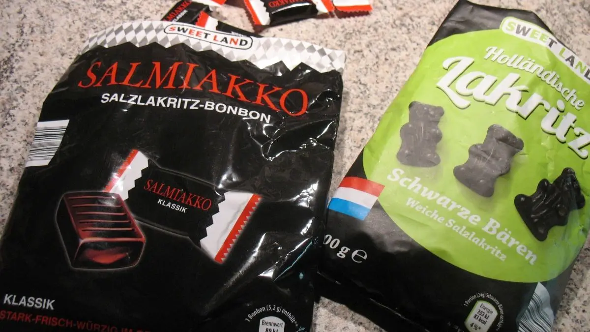 Zwei T&uuml;ten Lakritz liegen auf einer Tischoberfl&auml;che, w&auml;hrend um sie herum einige Lakritzbonbons verteilt sind.