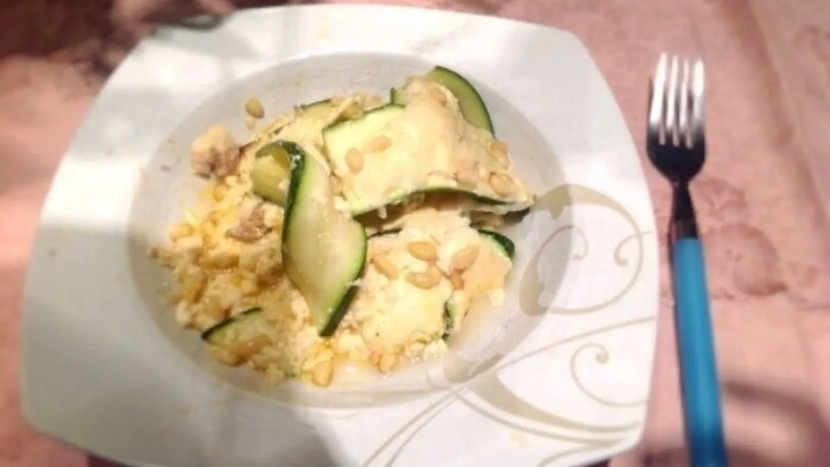 Der Zucchini-Hackfleisch-Auflauf liegt in einer wei&szlig;en Sch&uuml;ssel, umgeben von zarten Zucchinistreifen und Hackfleisch auf einem Tisch.