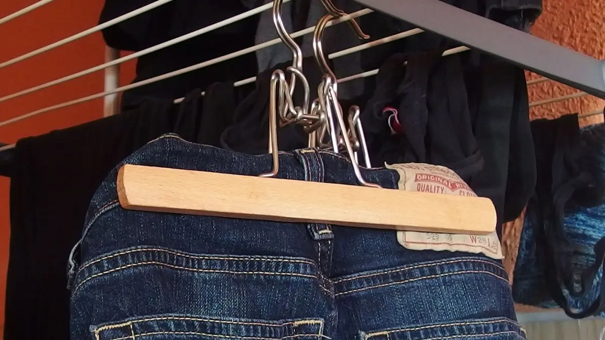 Jeans h&auml;ngen auf einem W&auml;schest&auml;nder, um schnell zu trocknen, im Hintergrund sind weitere Kleidungsst&uuml;cke sichtbar.