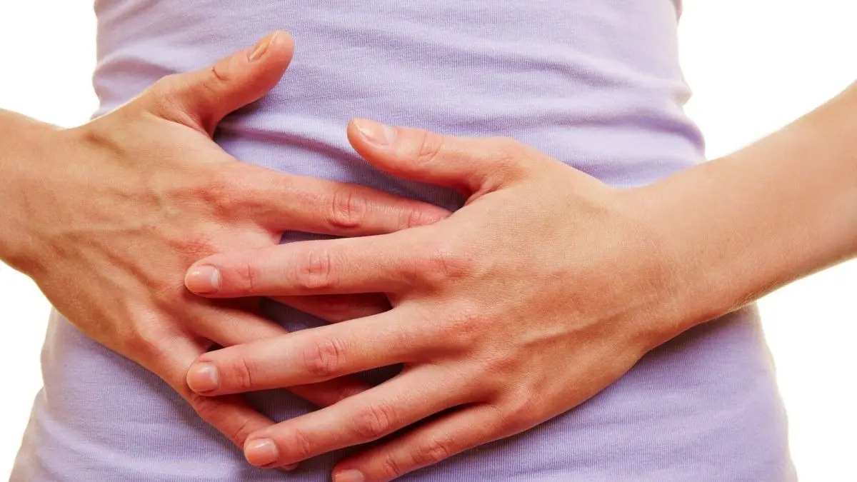 Eine Person h&auml;lt ihren Bauch, um Beschwerden nach einer Gallenblasen-OP zu lindern, in einem hellen, neutralen Hintergrund.
