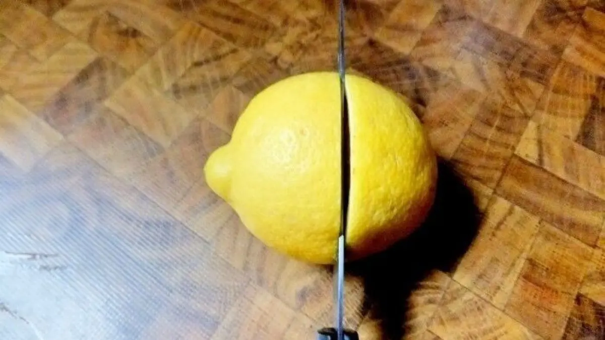 Eine Zitrone liegt auf einem Holzbrett, w&auml;hrend ein Messer sie diagonal schneidet, um Frische zu demonstrieren.