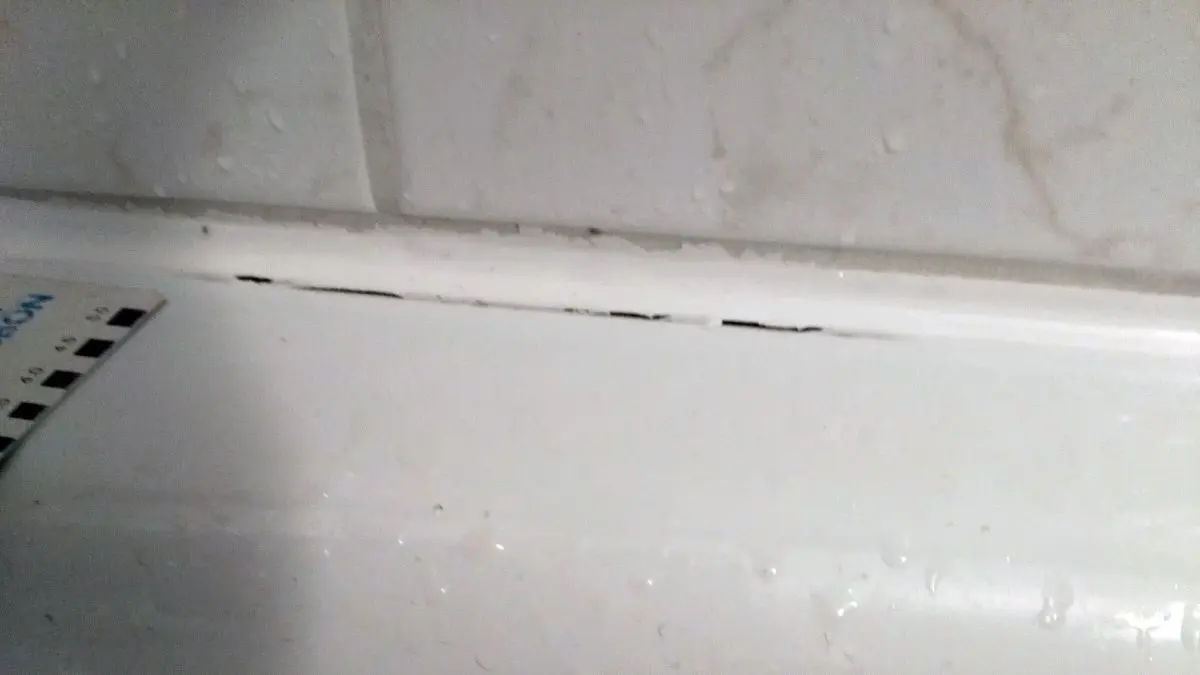 Risse zeigen sich an der Silikonfuge rund um die Badewanne, die feucht und besch&auml;digt aussieht.