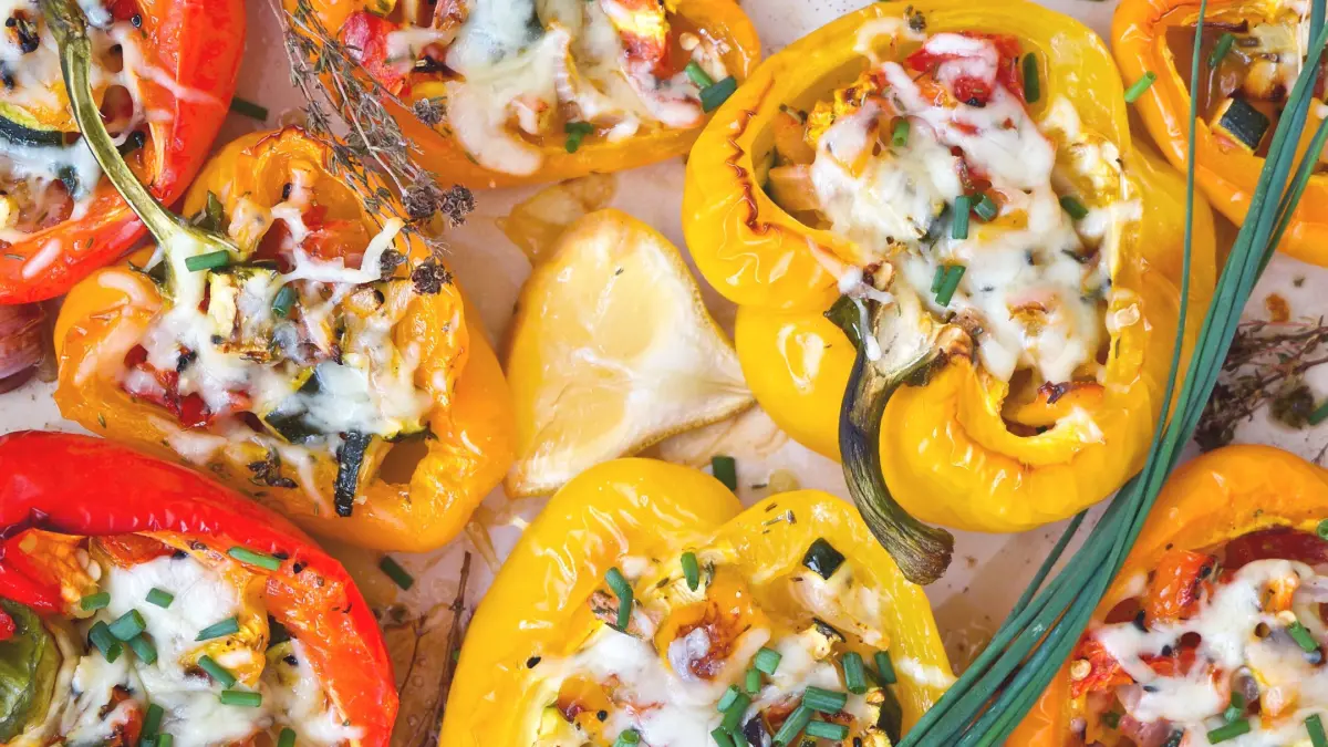 Gef&uuml;llte Paprika-H&auml;lften liegen auf einem Blech, &uuml;berbacken mit K&auml;se und garniert mit frischen Kr&auml;utern und Zitrone.