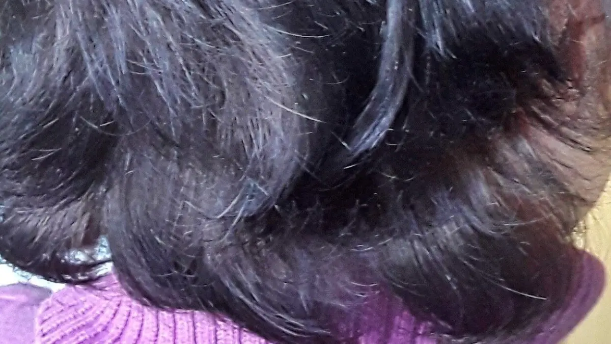 Dunkles, gesundes Haar in einem sanften Schwung f&auml;llt &uuml;ber den Nacken, getragen von einem lila Rollkragenpullover.