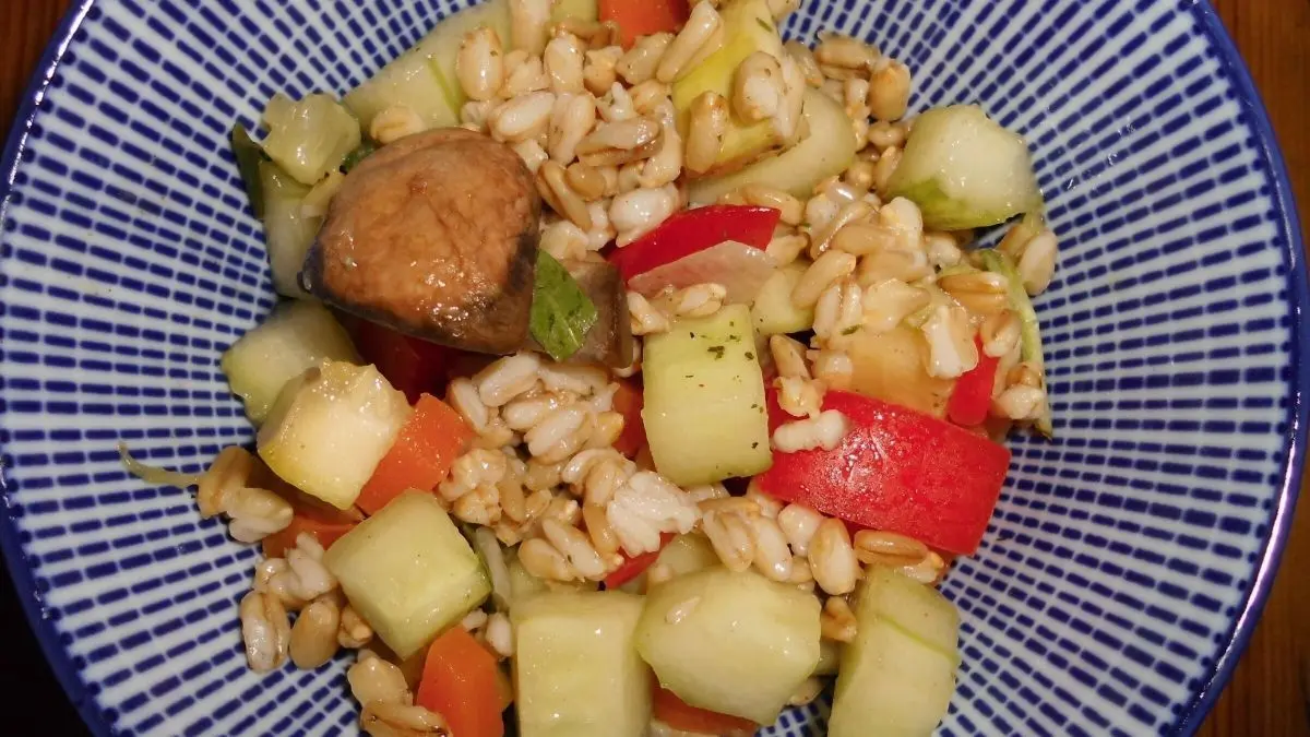Eine Sch&uuml;ssel mit buntem Salat aus ganzen Haferk&ouml;rnern, frischen Gem&uuml;sest&uuml;cken und einer kleinen Portion Fleisch im Mittelpunkt.