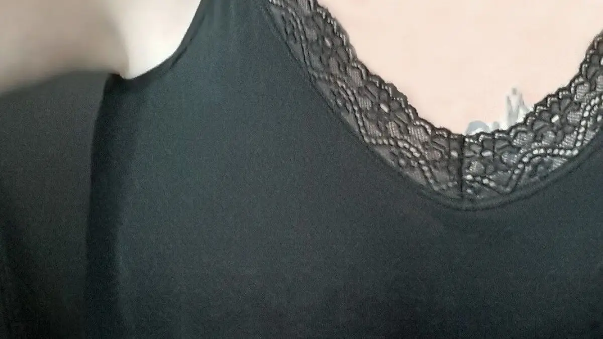 Ein schwarzes Top mit zartem Spitzensaum verdeckt dezent den Achselbereich und die Taille, betont aber die Silhouette.