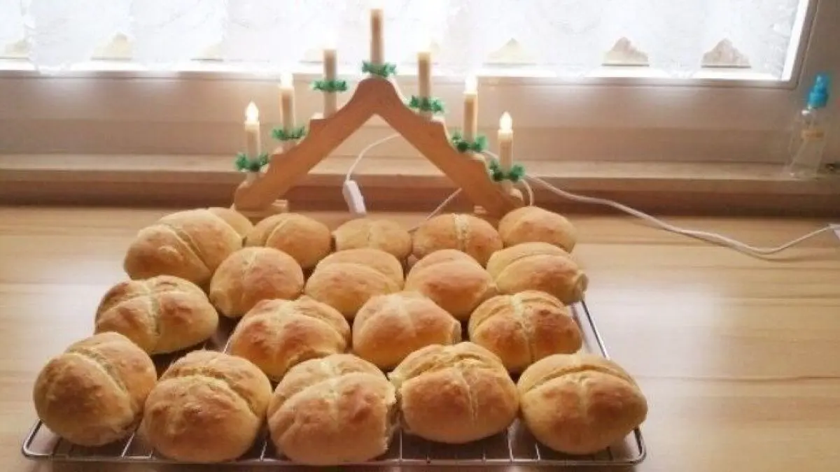 Frische Br&ouml;tchen liegen auf einem Holztablett, w&auml;hrend Kerzen in der Hintergrundbeleuchtung eine gem&uuml;tliche Atmosph&auml;re schaffen.