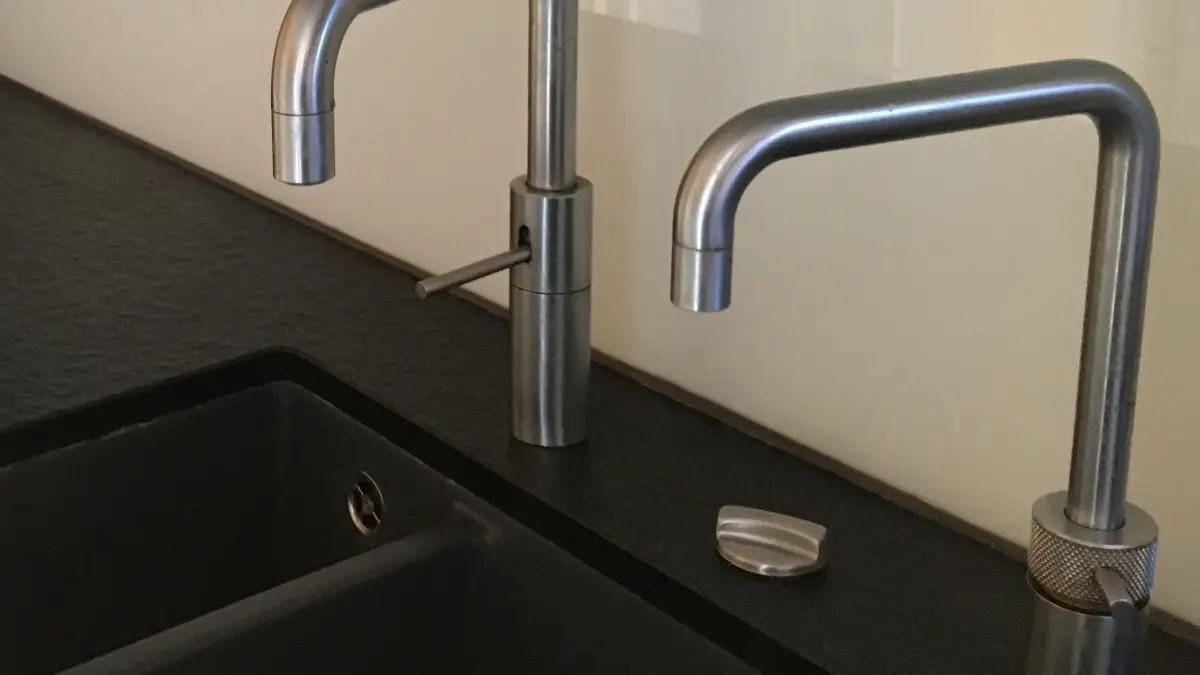 Zwei Wasserh&auml;hne stehen &uuml;ber einem dunklen Waschbecken und sind bereit, hei&szlig;es Wasser bereitzustellen.