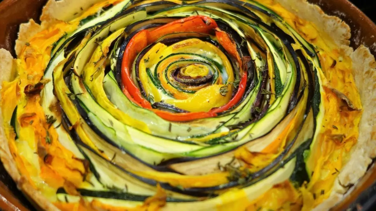 Eine farbenfrohe Gem&uuml;se-Spiral-Tarte liegt in einer runden Form und zeigt spiralf&ouml;rmig angeordnete, frische Gem&uuml;sestreifen.