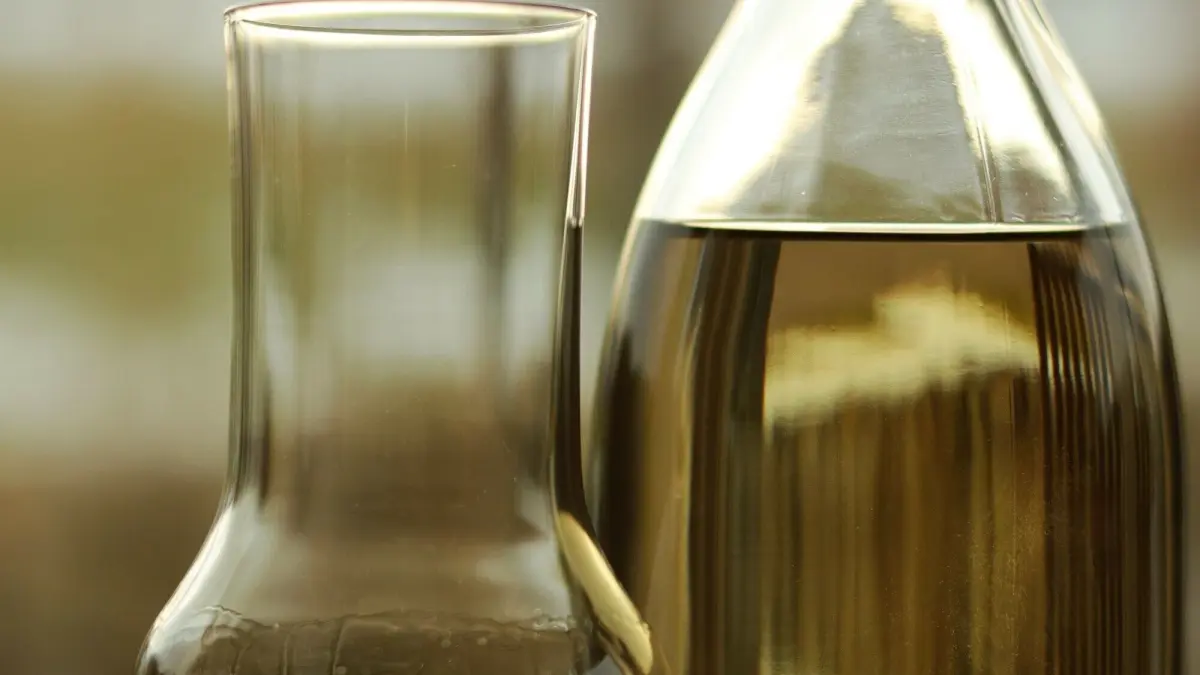 Eine Glasflasche mit leichtem, goldenem Getr&auml;nk steht neben einem hohen, schmalen Glas, das bereit ist zum Servieren.