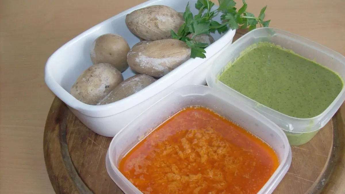 Papas arrugadas liegen zusammen mit Mojo rojo und Mojo verde auf einem Holzbrett, bereit zum Servieren.