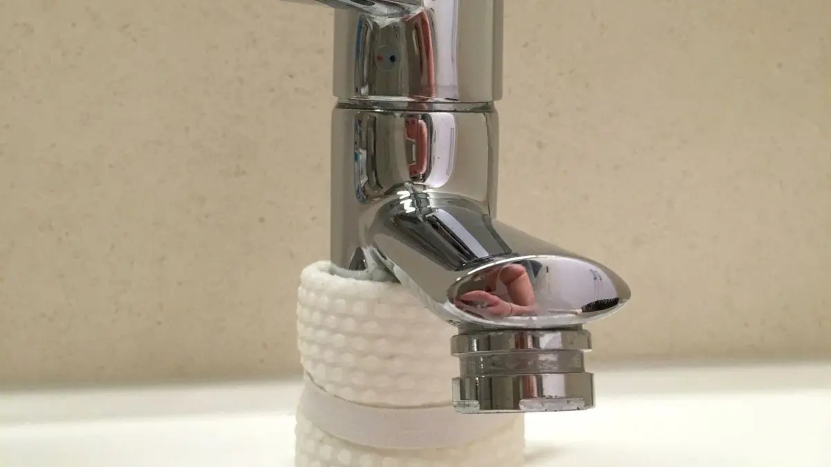Ein gl&auml;nzender Wasserhahn tropft und steht auf einem Waschbeckenrand, umgeben von einer schlichten Wand.