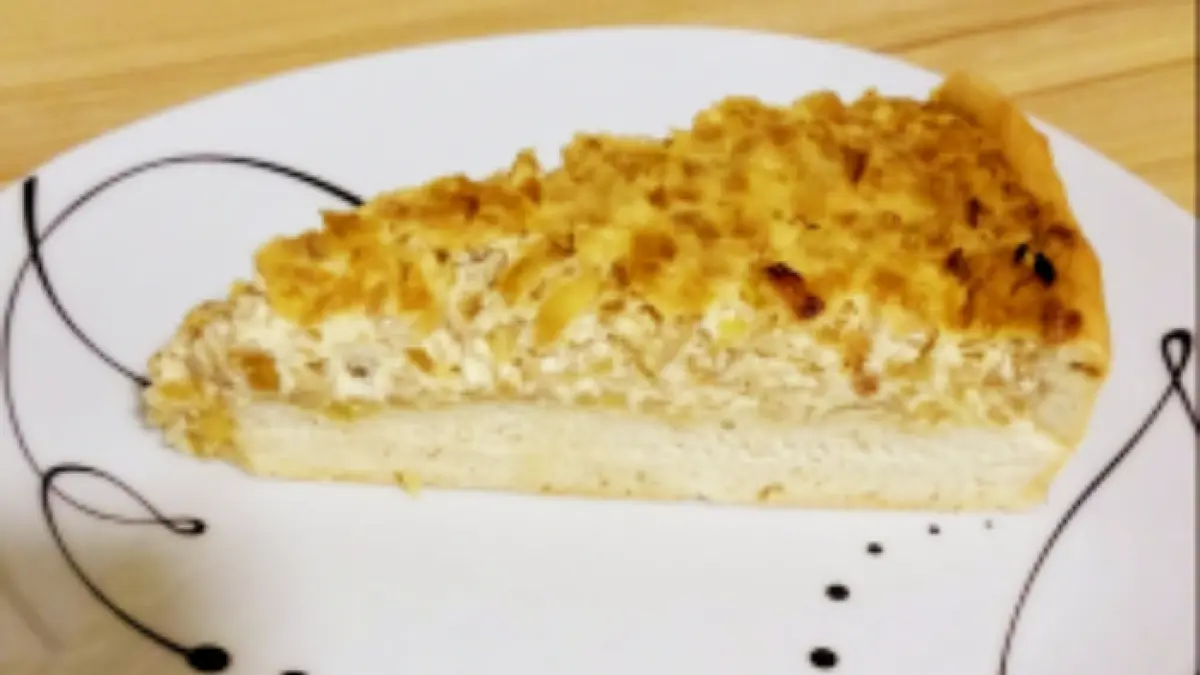Ein St&uuml;ck Zwiebelkuchen mit Schmand liegt auf einem dekorativen Teller und ruht auf einer Holzoberfl&auml;che.
