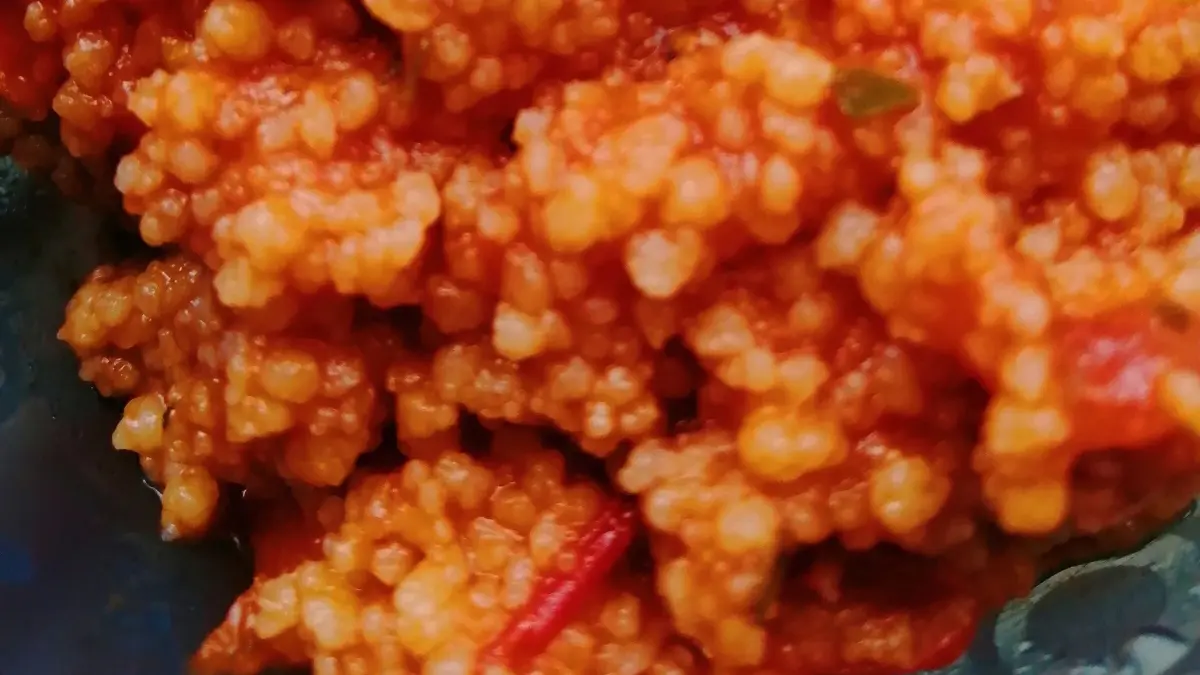 Couscous erscheint in einer schmackhaften Mischung mit Tomaten und Paprika, serviert in einer durchsichtigen Sch&uuml;ssel.
