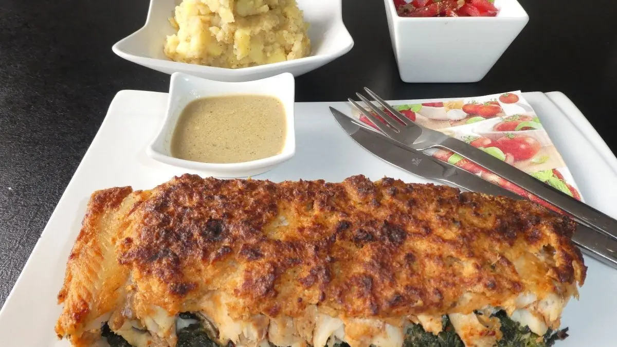 &Uuml;berbackener Fisch mit knuspriger Kruste liegt auf Blattspinat, serviert mit Beilagen in kleinen Schalen.