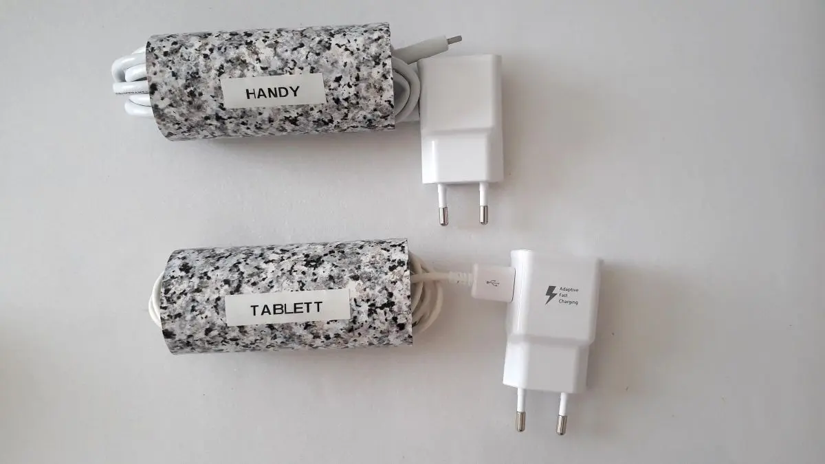 Zwei Ladekabel sind ordentlich verstaut in h&uuml;bschen H&uuml;llen, verbunden mit wei&szlig;en Netzteilen auf einem hellen Untergrund.