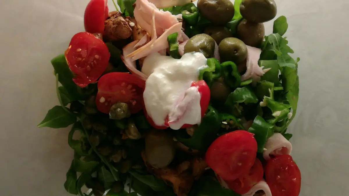 Frischer Rucola-Salat wird mit Kirschtomaten, Pfifferlingen und Putenschinken in einer Sch&uuml;ssel angerichtet.