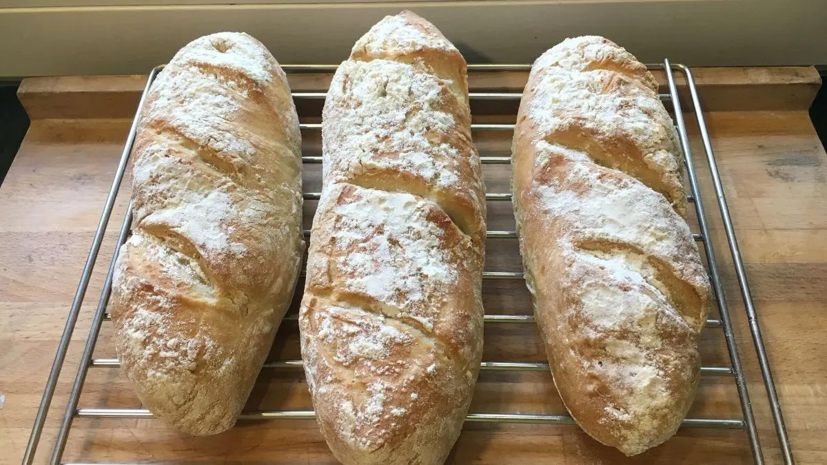 Drei frisch gebackene Baguettes ruhen auf einem Gitterrost in einer hellen K&uuml;che, bereit zum Servieren.